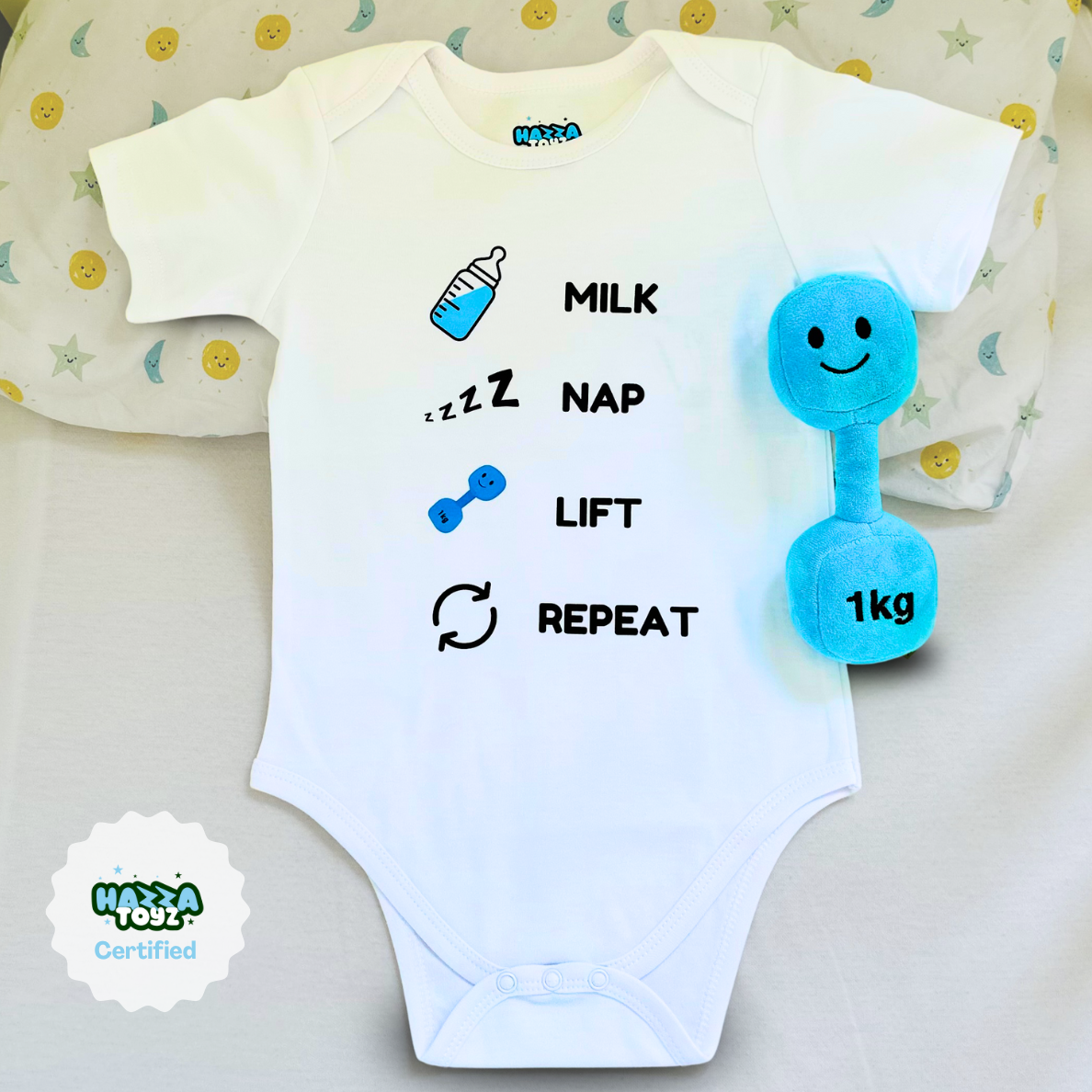 Flat lay of Hazza Toyz Milk Nap Lift Repeat white baby bodysuit paired with Mystic Blue 1kg plush dumbbell – funny gym-themed baby outfit and toy gift set