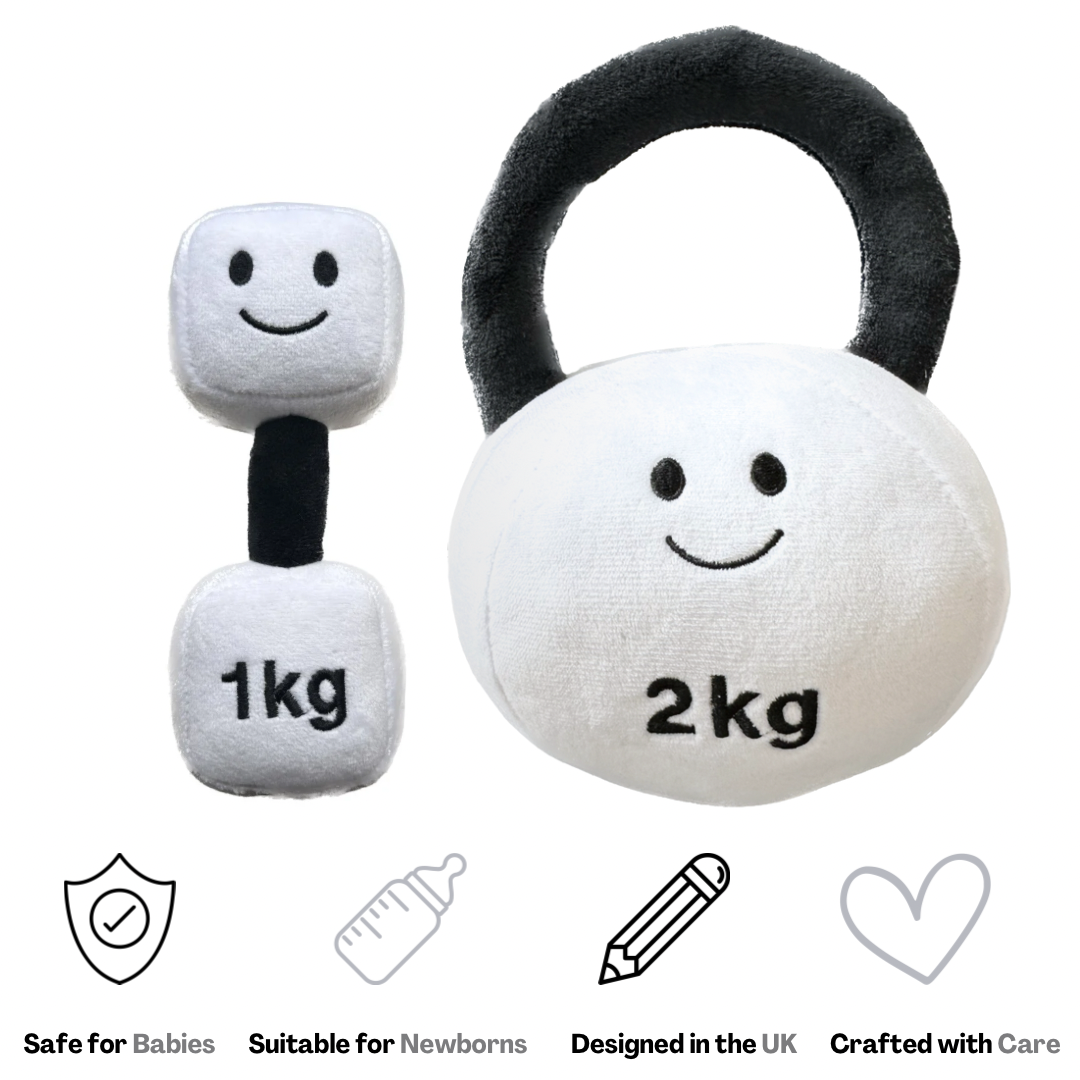 A set of two plush baby toys designed to look like a dumbbell and a kettlebell, with smiling faces on them. The dumbbell is smaller, and the kettlebell is larger, both in a white and black color scheme, with text indicating their weights as 1kg and 2kg respectively.