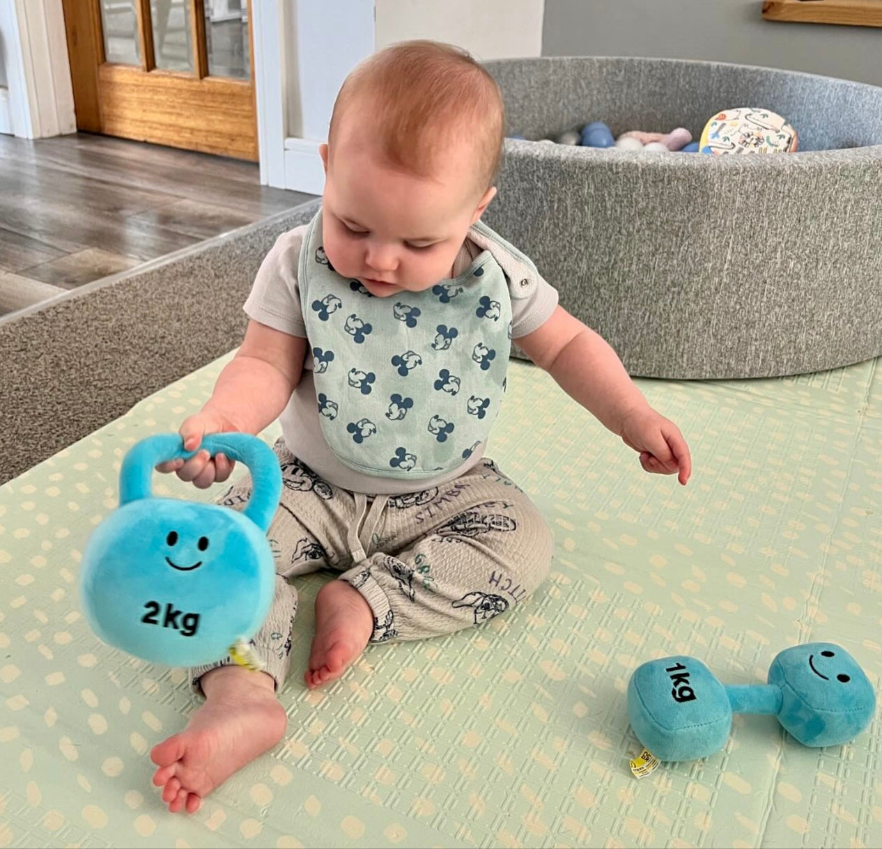 Baby playing with Hazza Toyz Mystic Blue plush kettlebell, promoting sensory development and motor skills through fun interactive play