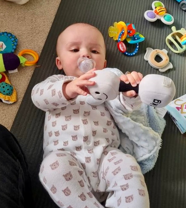 Baby lying on play mat in bear-print sleepsuit holding white plush dumbbell with black handle