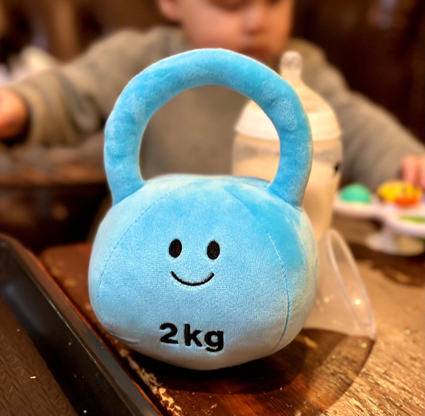Mystic Blue kettlebell with a blurry background in a coffee shop, highlighting the portability and playful design of Hazza Toyz fitness-inspired toys for toddlers.