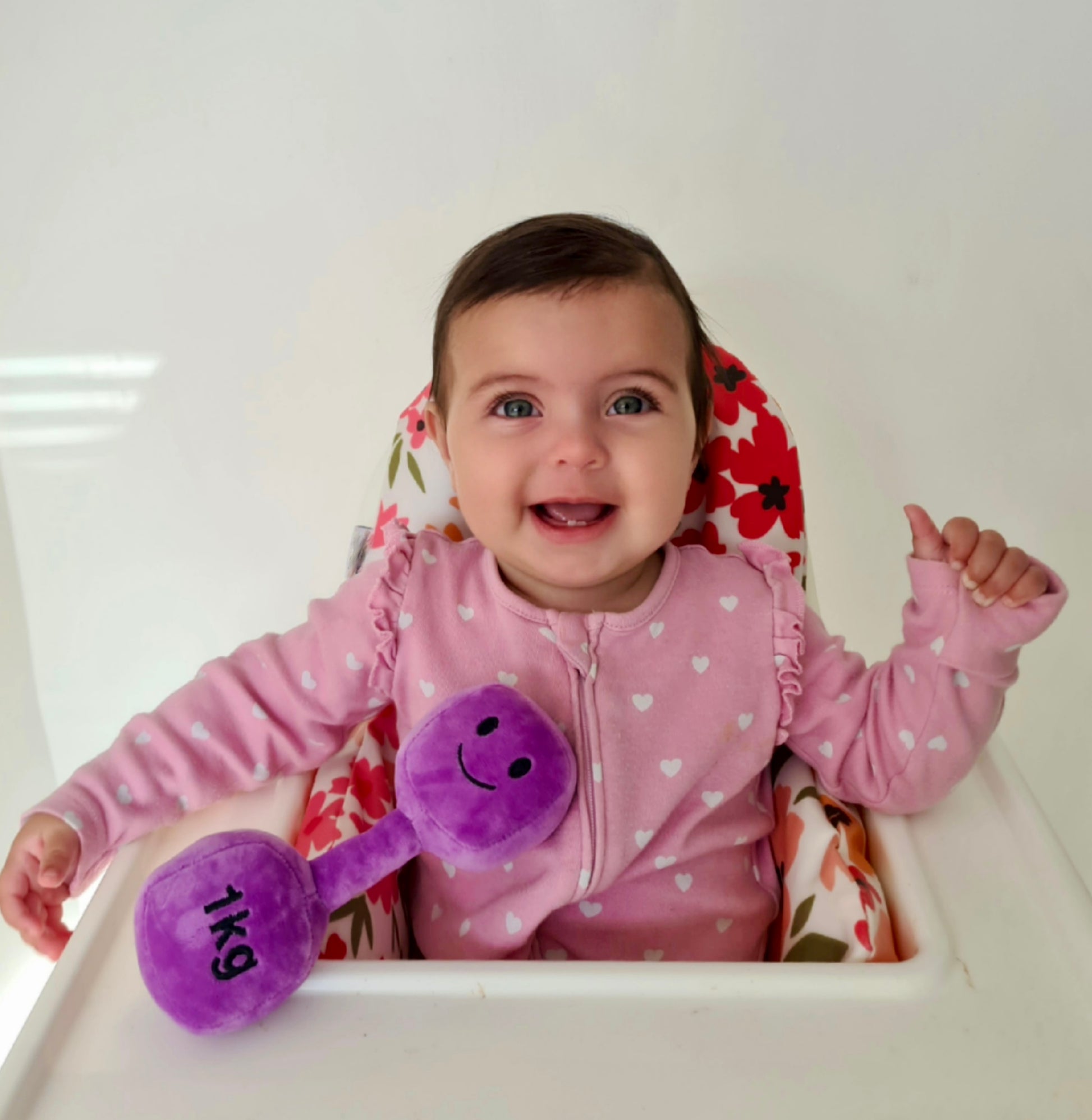 Baby in highchair holding Hazza Toyz Lavender Purple plush dumbbell, enjoying playtime