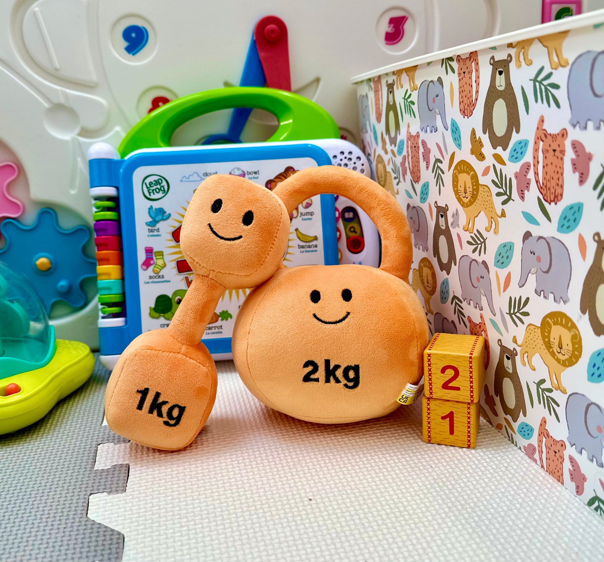 Hazza Toyz Apricot Orange dumbbell and kettlebell on playmat, showcased as a hero image for sensory play and motor skill development