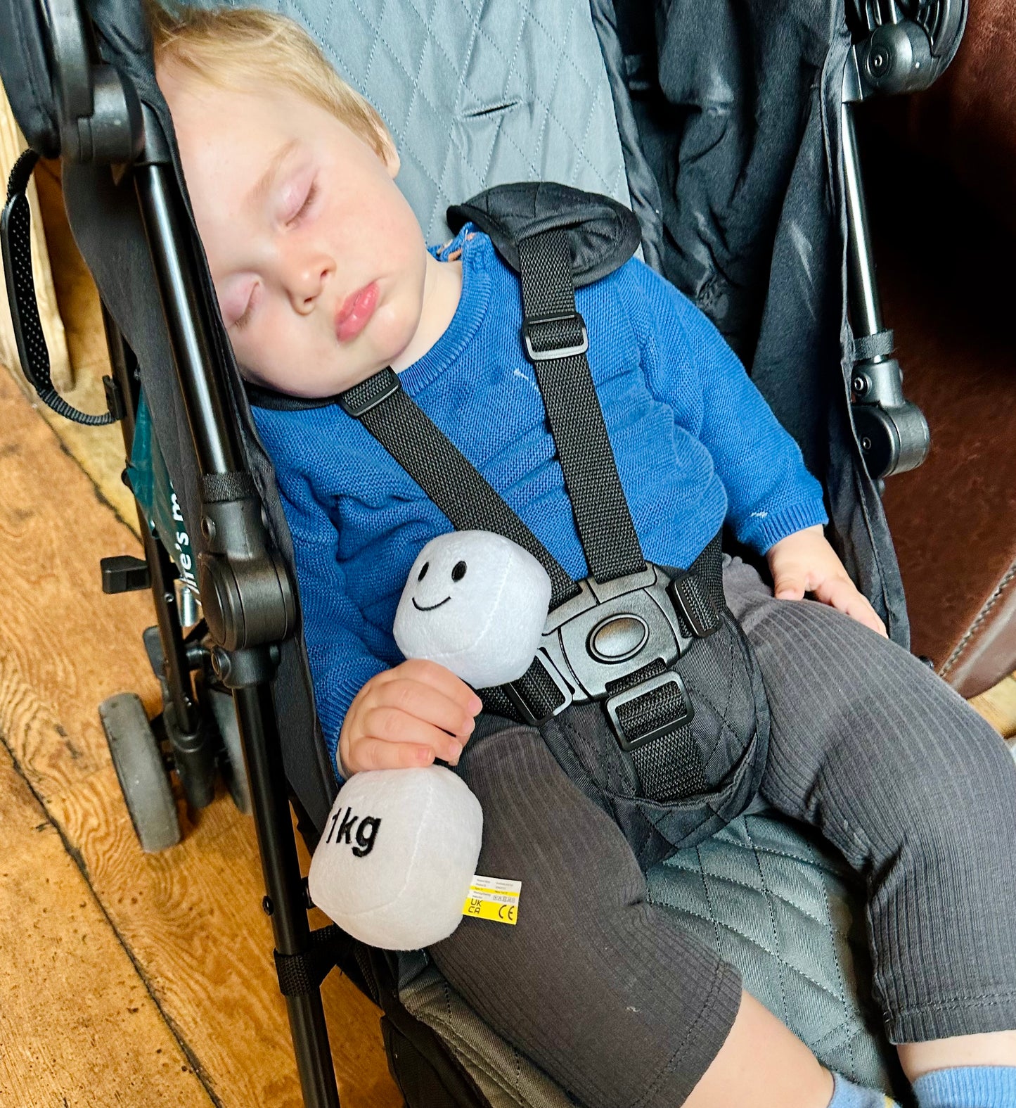 Baby asleep in pram at coffee shop, holding Hazza Toyz Lamby Black and White dumbbell, enjoying a cosy and restful moment