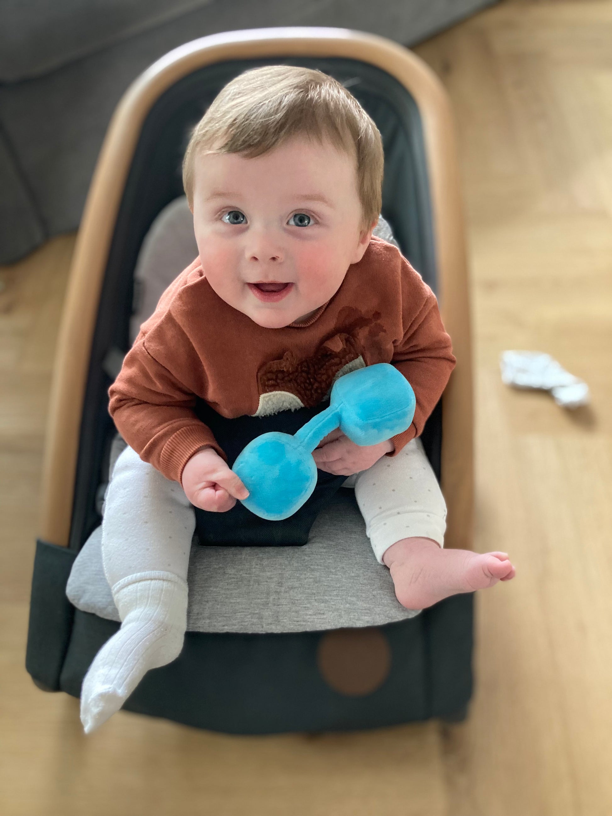 Cute baby in car seat holding Hazza Toyz Mystic Blue dumbbell, smiling and enjoying sensory play during travel