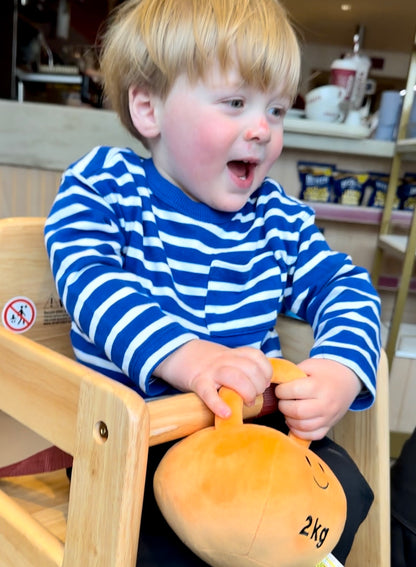 Baby with Hazza Toyz Apricot Orange kettlebell in a coffee shop, enjoying sensory play in a cosy setting