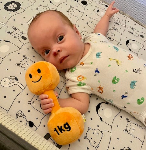 Cute baby holding Hazza Toyz Apricot Orange dumbbell, engaging in playful sensory exploration and motor skill development