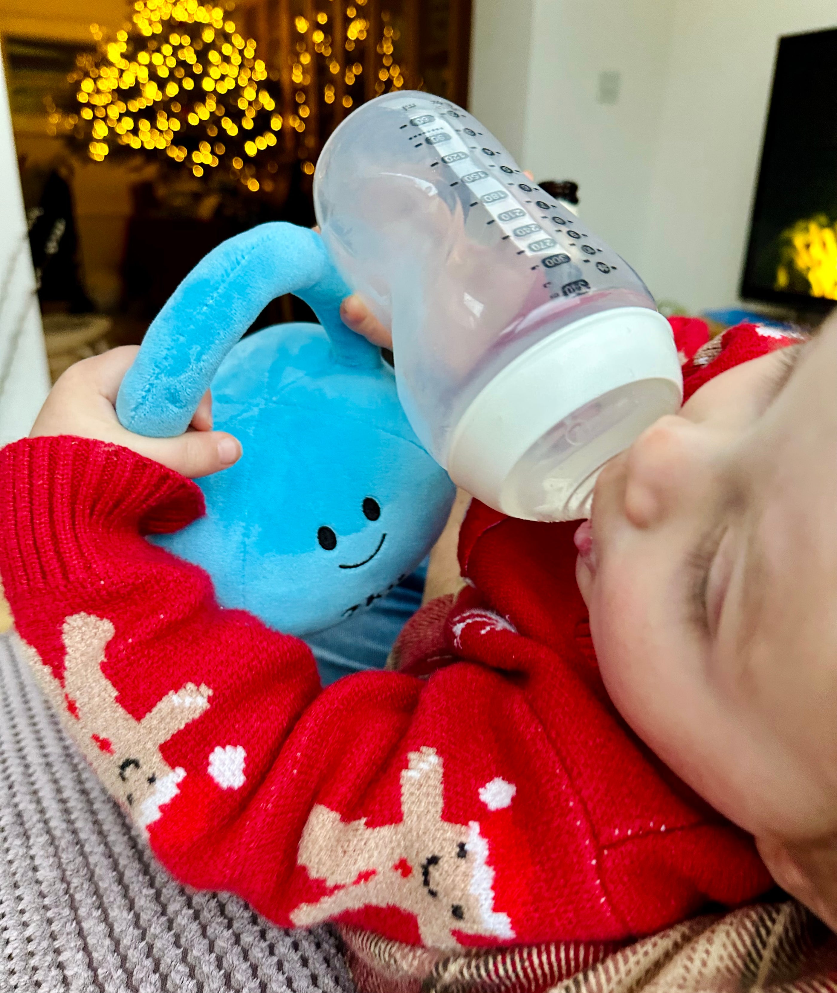 Baby drinking milk while holding a Mystic Blue kettlebell during Christmas time, capturing a festive moment with Hazza Toyz fitness-inspired toys for toddlers.
