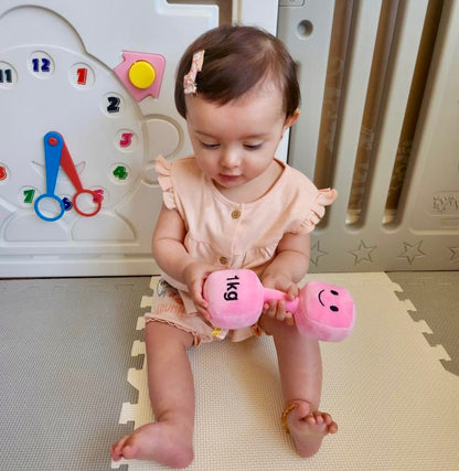 Baby girl holding Hazza Toyz Candy Chateau Pink dumbbell, enjoying playful interaction and developing motor skills