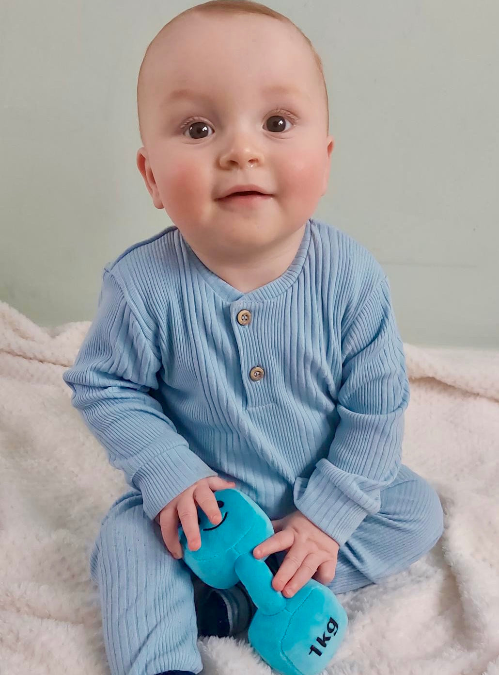 Baby holding Hazza Toyz dumbbell and looking at camera, enjoying playful interaction and sensory development