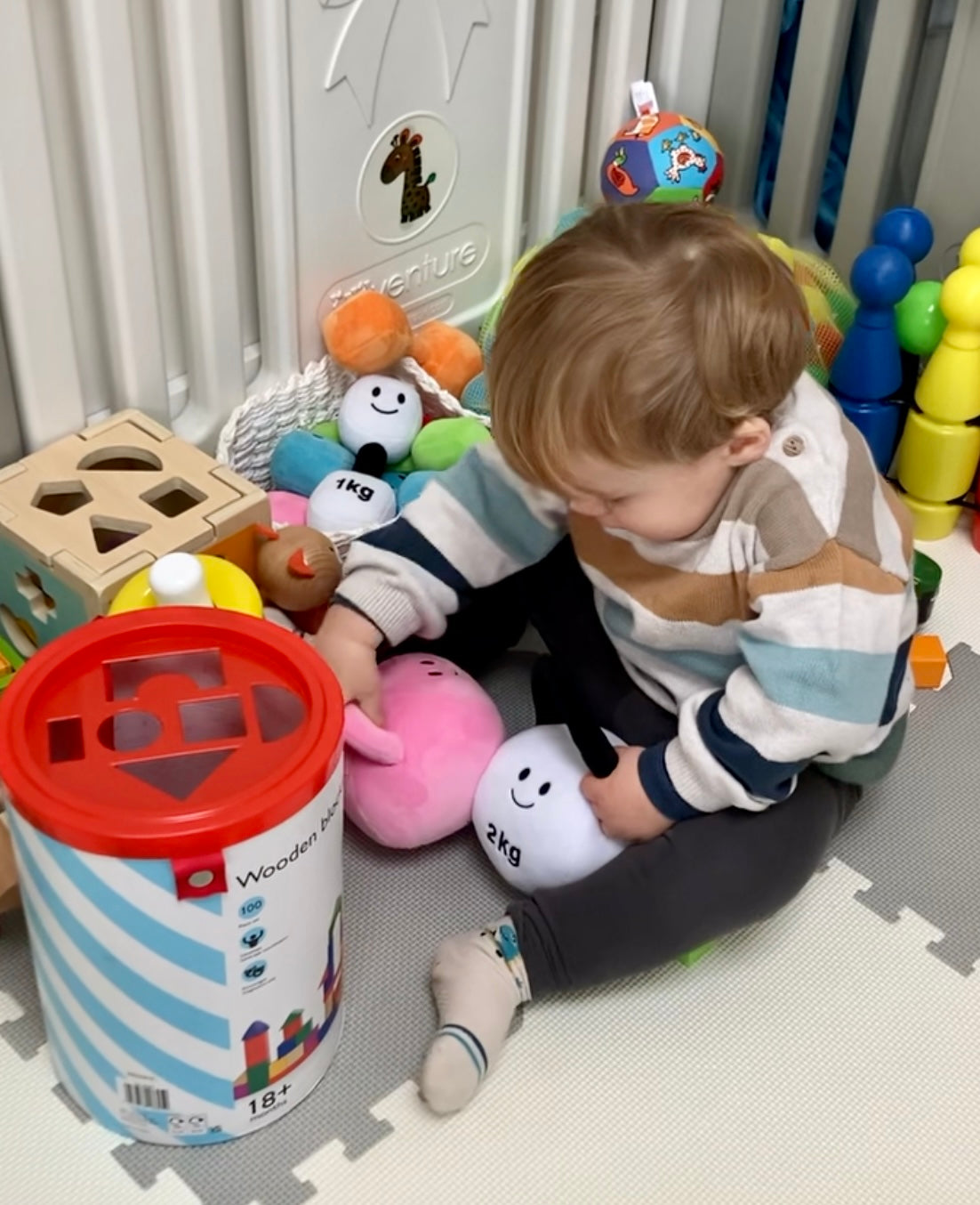 Baby holding Hazza Toyz Candy Chateau Pink and Lamby Black and White kettlebells, enjoying sensory play and motor skill development