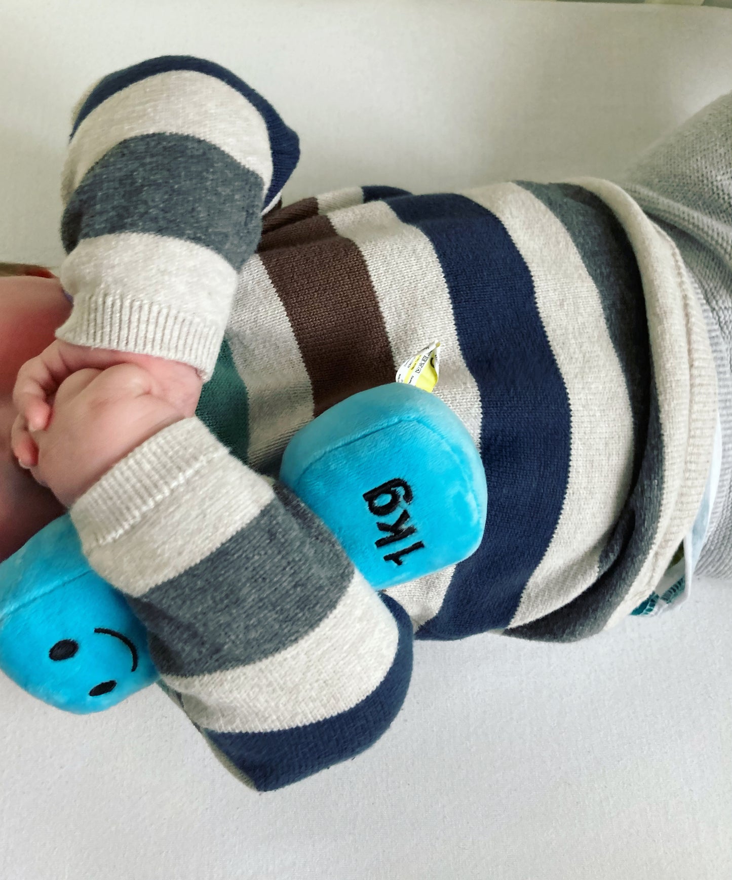 Baby hugging a blue dumbbell in a cot, showing a cosy moment with Hazza Toyz fitness-inspired toys for toddlers