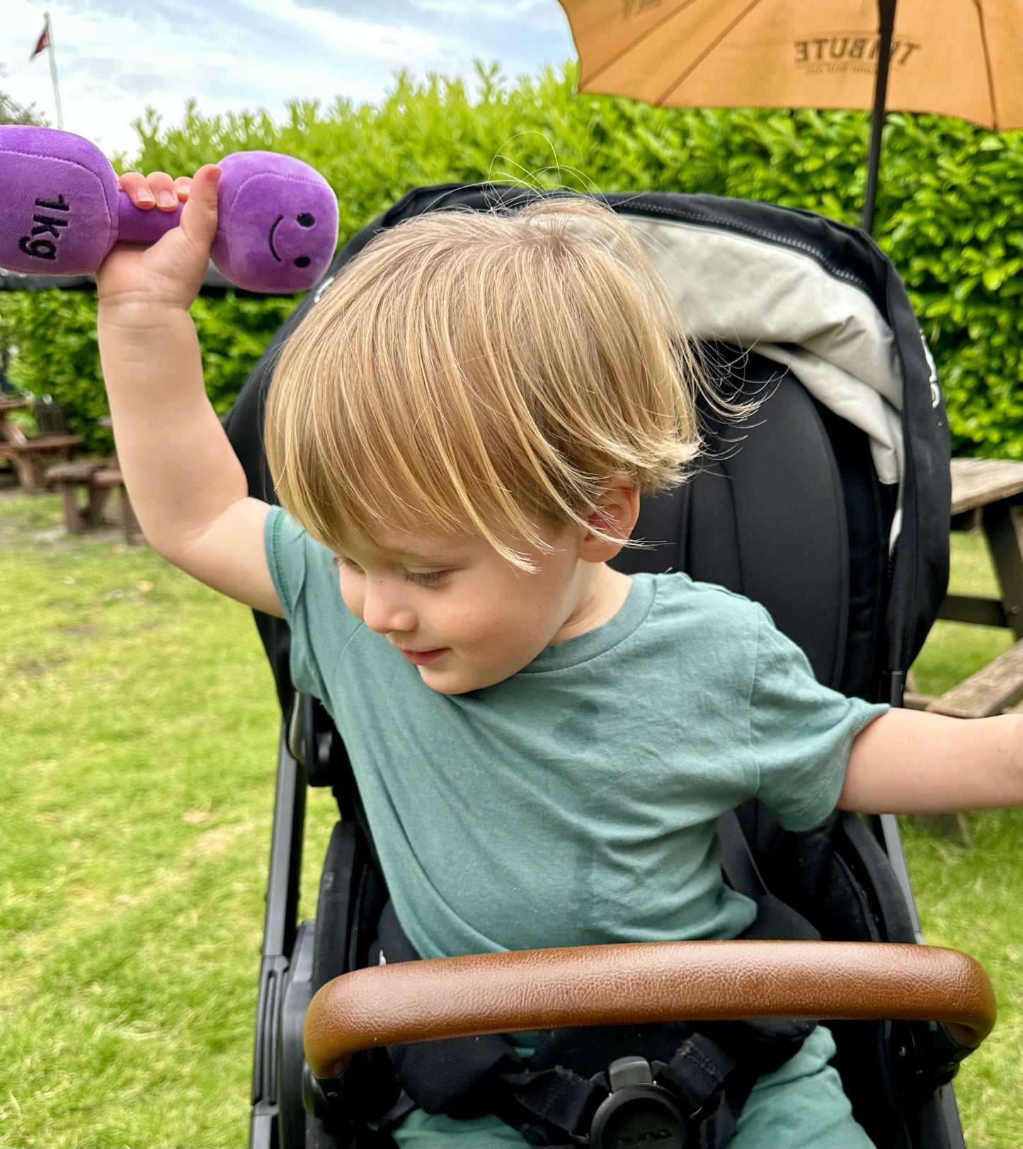 Baby laughing in pram while holding Hazza Toyz Lavender Purple dumbbell, enjoying playful sensory engagement during a stroll