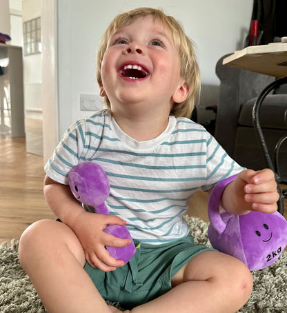 Baby laughing while playing with Hazza Toyz Lavender Purple kettlebell and dumbbell, enjoying interactive sensory play and motor skill development