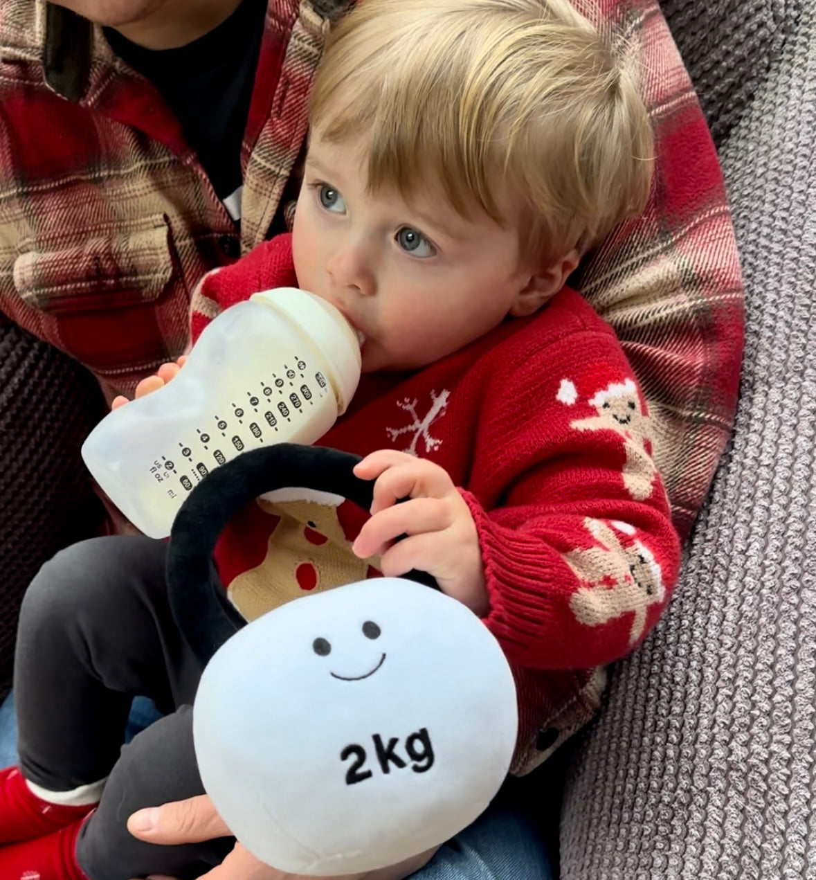 Baby on dad's lap drinking milk while holding Hazza Toyz Lamby Black and White kettlebell, enjoying a comforting and playful moment