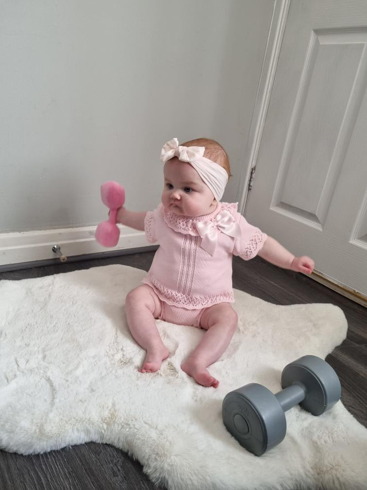 Baby on rug holding Hazza Toyz Candy Chateau Pink dumbbell, engaging in sensory play and early motor skill development