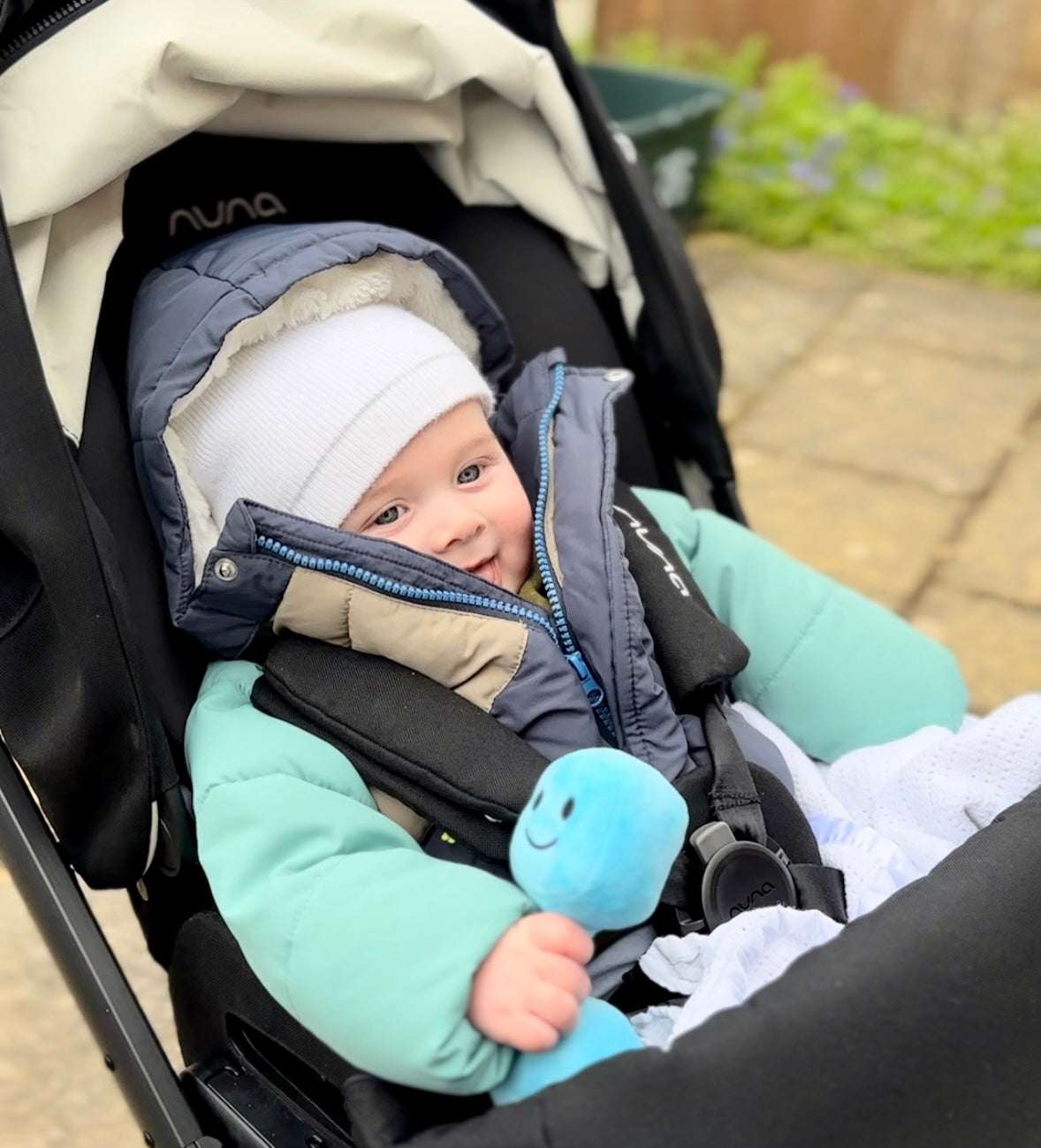 Baby in pram smiling while holding Hazza Toyz Mystic Blue dumbbell, enjoying playful sensory engagement on a walk