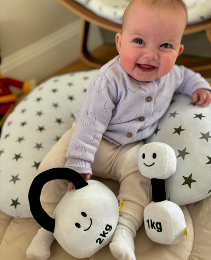 Baby smiling while playing with Hazza Toyz Lamby Black and White dumbbell and kettlebell, enjoying sensory play and motor skill development