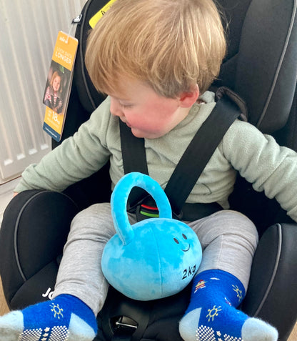 Baby in travel seat holding Hazza Toyz Mystic Blue kettlebell, enjoying sensory play during a car ride