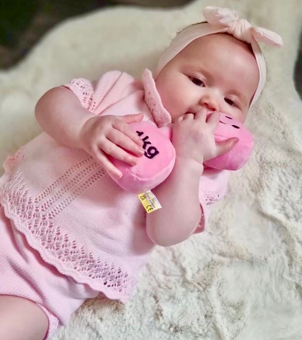 Baby with pink headband cuddling Hazza Toyz Candy Chateau Pink dumbbell, enjoying a soft and comforting playtime moment