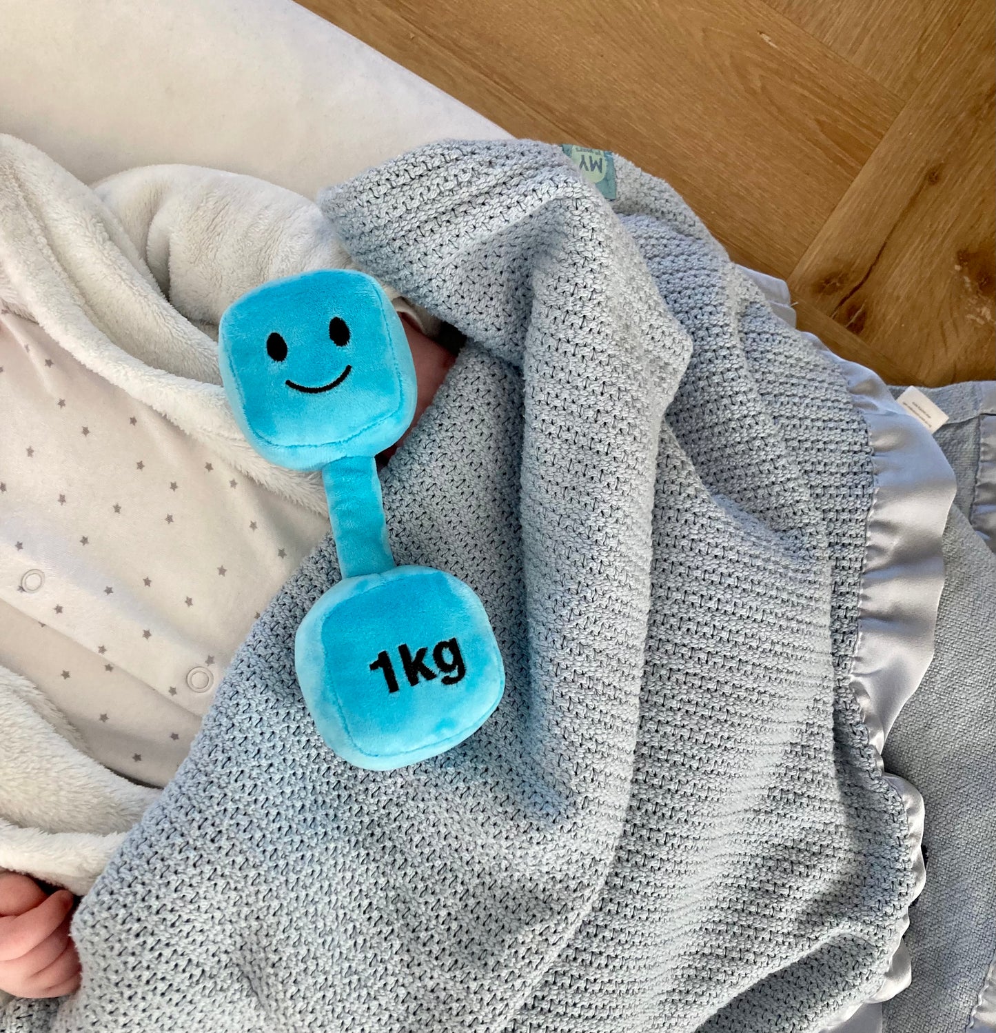 Blue dumbbell resting next to a sleeping baby in a cot, illustrating peaceful rest after active play with Hazza Toyz fitness-inspired toys for toddlers.