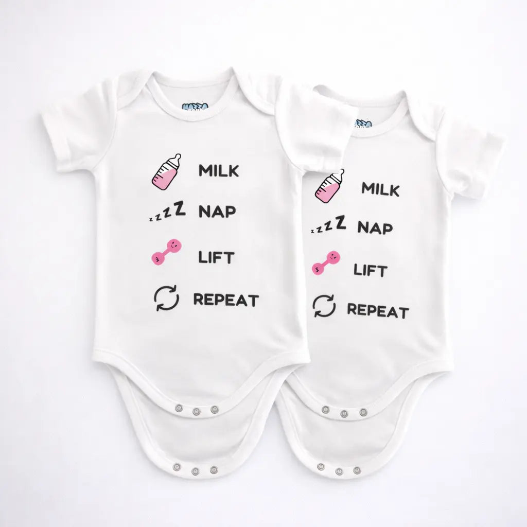 Two white and pink baby bodysuits with milk nap lift repeat text and small bottle and dumbbell graphics displayed on a grey background