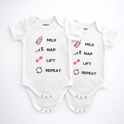 Two white and pink baby bodysuits with milk nap lift repeat text and small bottle and dumbbell graphics displayed on a grey background