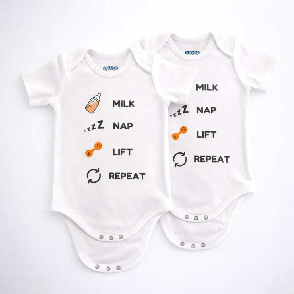 Two white baby bodysuits with milk nap lift repeat text and small bottle and dumbbell graphics displayed on a grey background