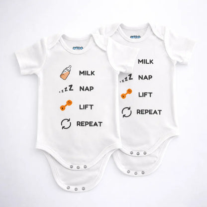 Two white baby bodysuits with milk nap lift repeat text and small bottle and dumbbell graphics displayed on a grey background