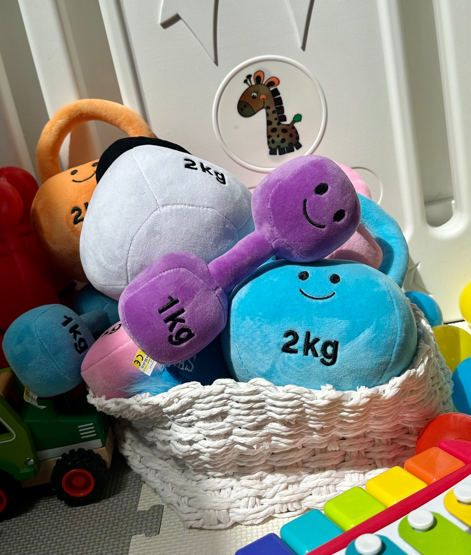 Hazza Toyz dumbbells and kettlebells in a basket, showcasing colorful plush toys for babies and toddlers designed for sensory play and motor skill development