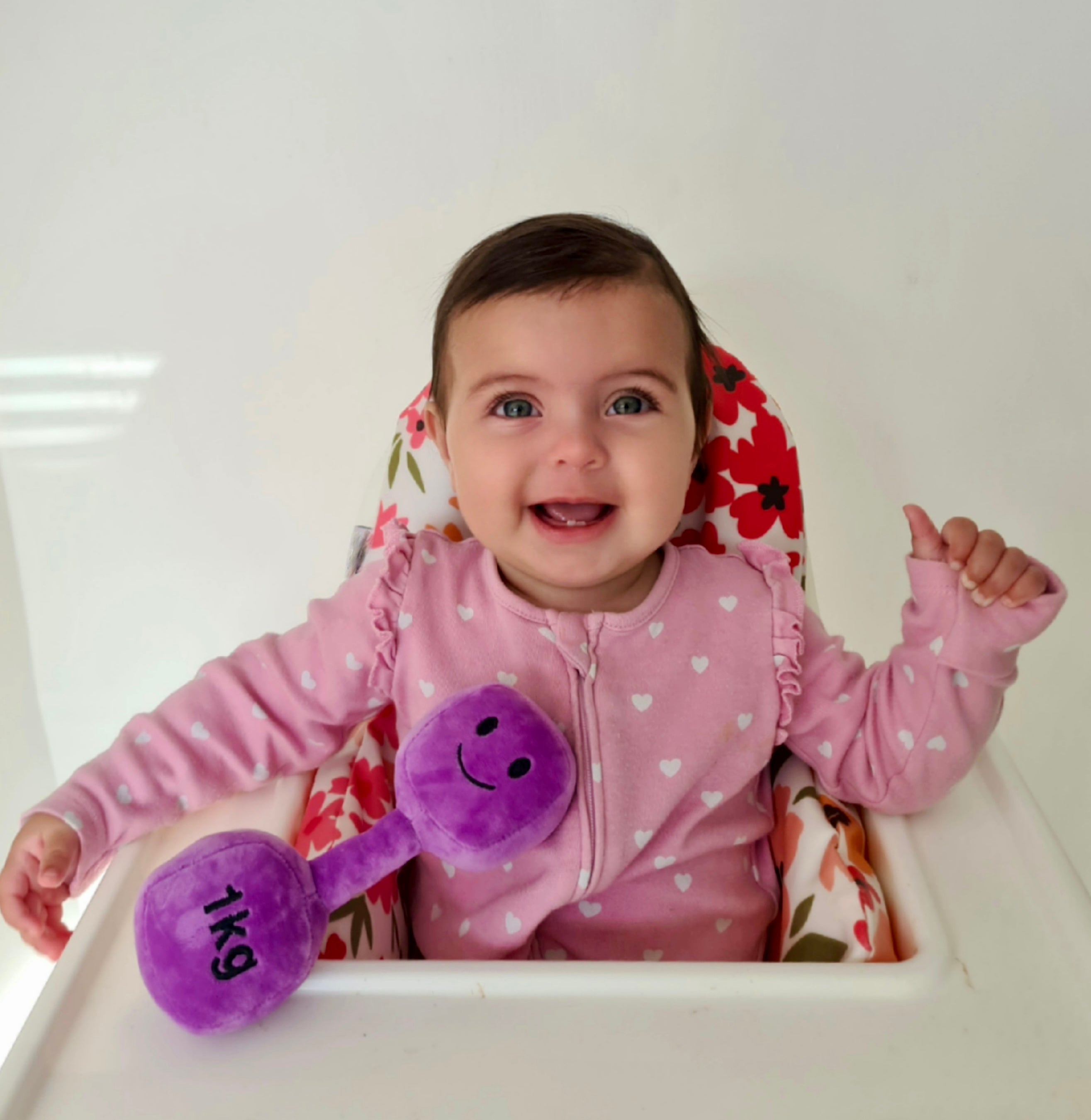 Baby in highchair holding Hazza Toyz Lavender Purple plush dumbbell, enjoying playtime