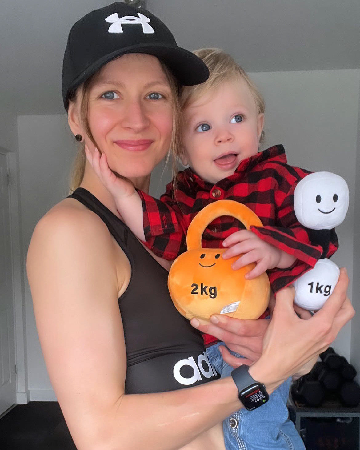 Mum and toddler playing together with an Apricot Orange kettlebell and a Lamby Black and White dumbbell, sharing joyful moments with Hazza Toyz fitness-inspired toys for toddlers.