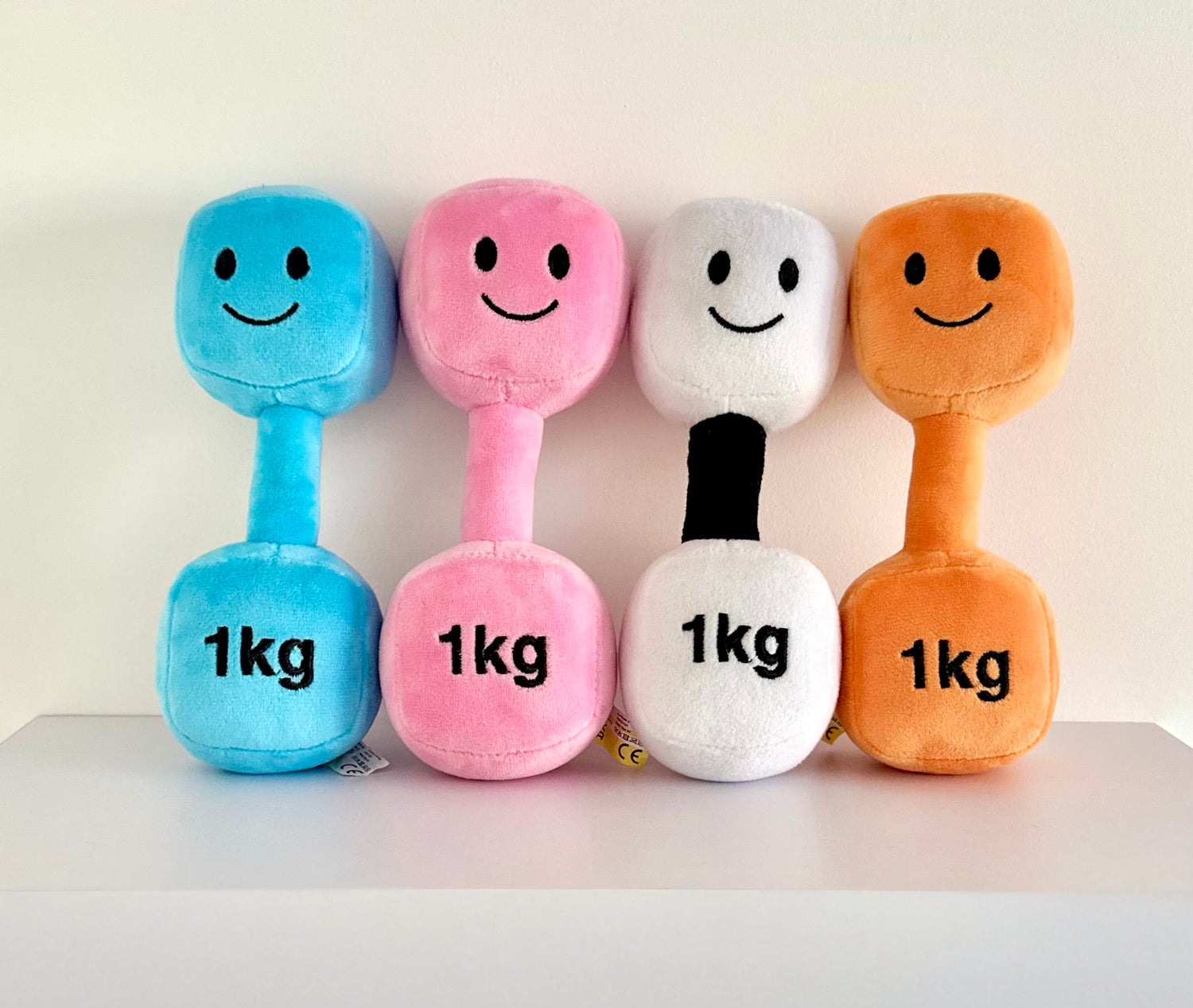 Hazza Toyz dumbbells in Candy Chateau Pink, Mystic Blue, Lamby Black and White, and Apricot Orange arranged in a line on a shelf with white background, showcasing colourful sensory toys