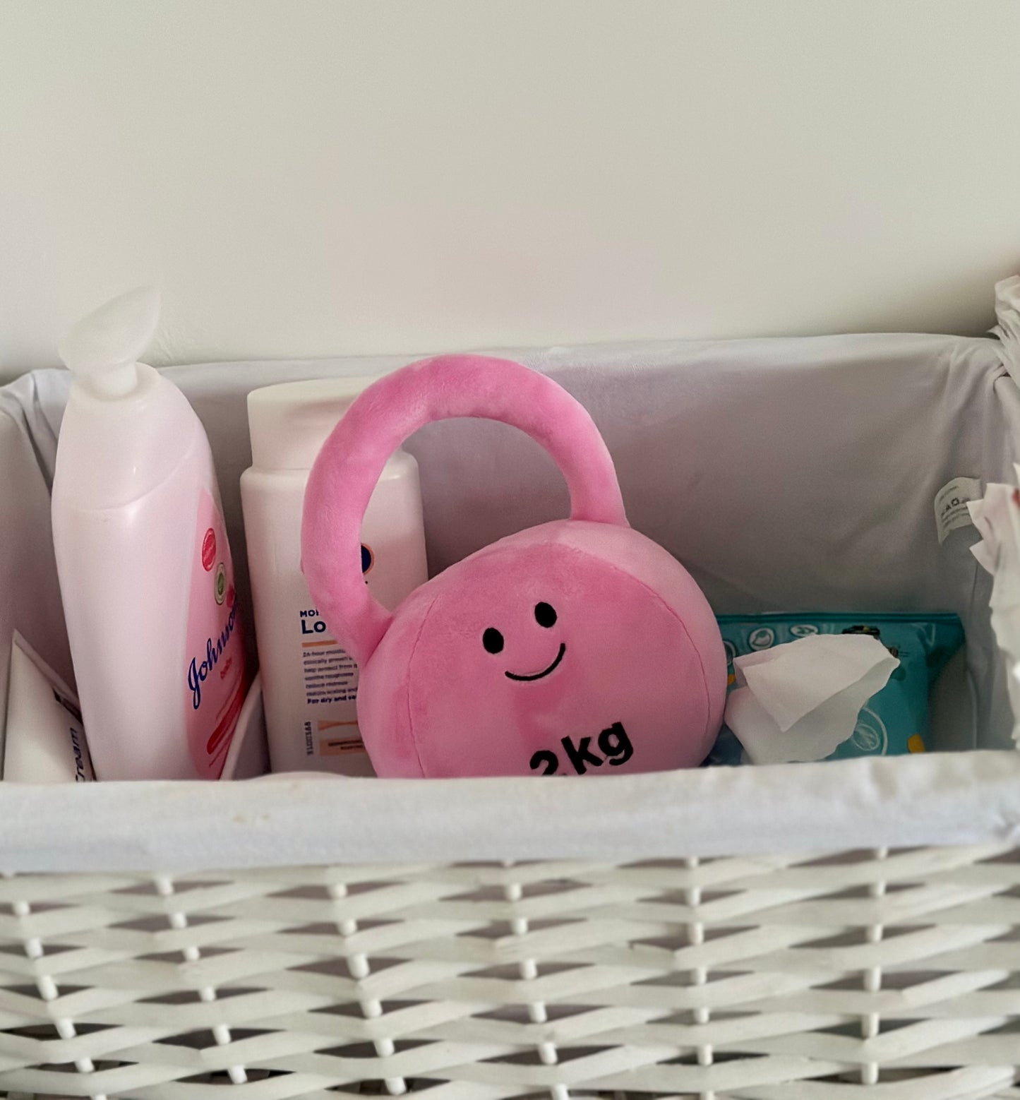 Hazza Toyz Candy Chateau Pink kettlebell in a box or basket with other baby essentials like nappies, creating a playful and practical arrangement