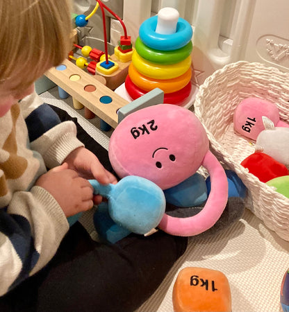 Toddler on playmat with Hazza Toyz Candy Chateau Pink kettlebell, engaging in sensory play and motor skill development