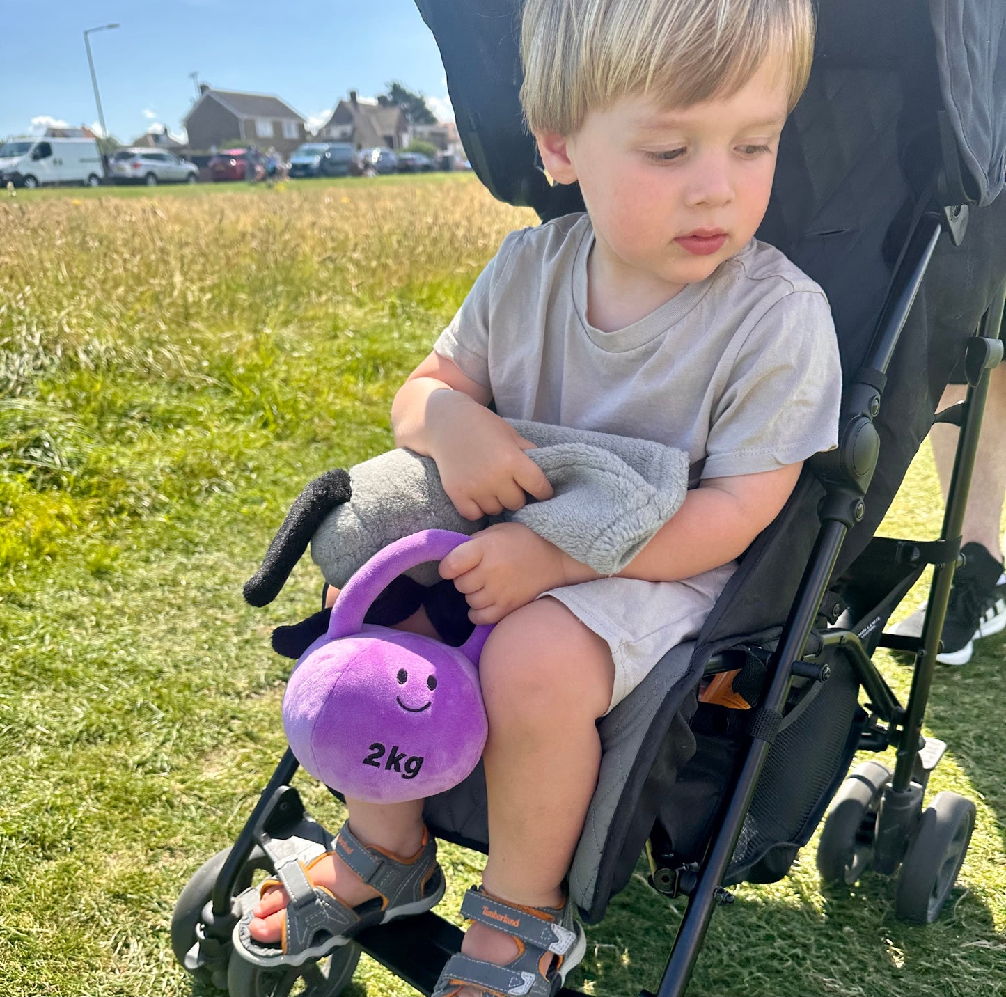 Baby in pram with Hazza Toyz Lavender Purple kettlebell at the seaside, enjoying sensory play in a scenic outdoor setting