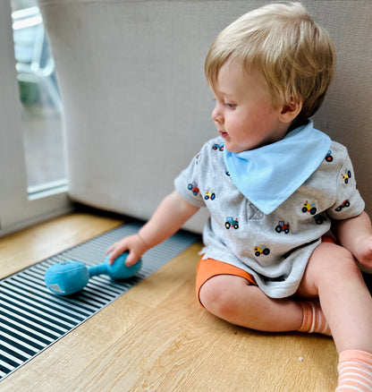 Toddler wearing blue bib reaching for Hazza Toyz Mystic Blue dumbbell, engaging in sensory play and developing motor skills