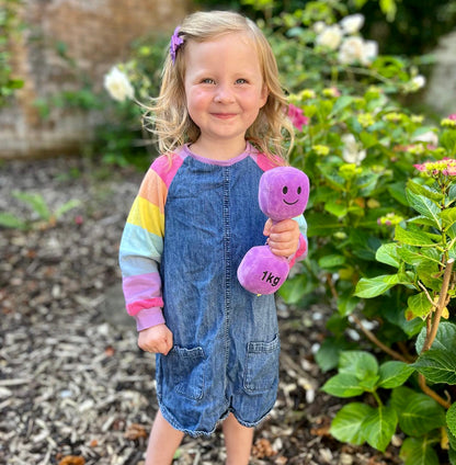 Toddler smiling in garden while holding Hazza Toyz Lavender Purple dumbbell, enjoying outdoor sensory play and physical activity