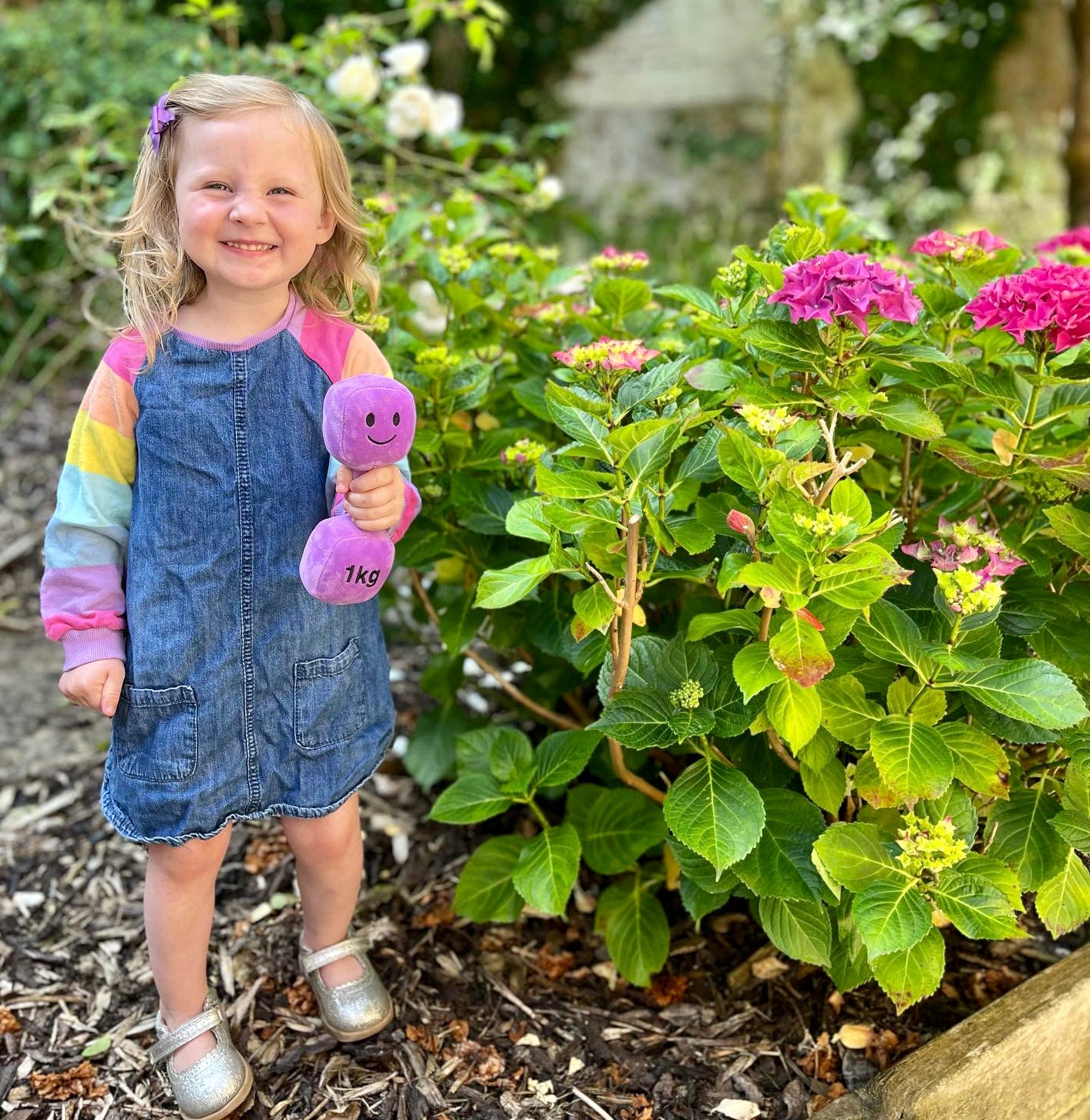 Toddler playing in garden with Hazza Toyz Lavender Purple dumbbell, engaging in outdoor sensory play and motor skill development