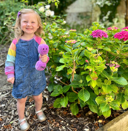 Toddler playing in garden with Hazza Toyz Lavender Purple dumbbell, engaging in outdoor sensory play and motor skill development