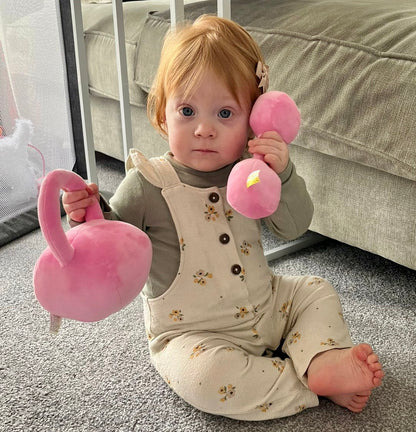 Toddler holding Hazza Toyz Candy Chateau Pink dumbbell to her ear and a pink kettlebell, enjoying playful sensory interaction