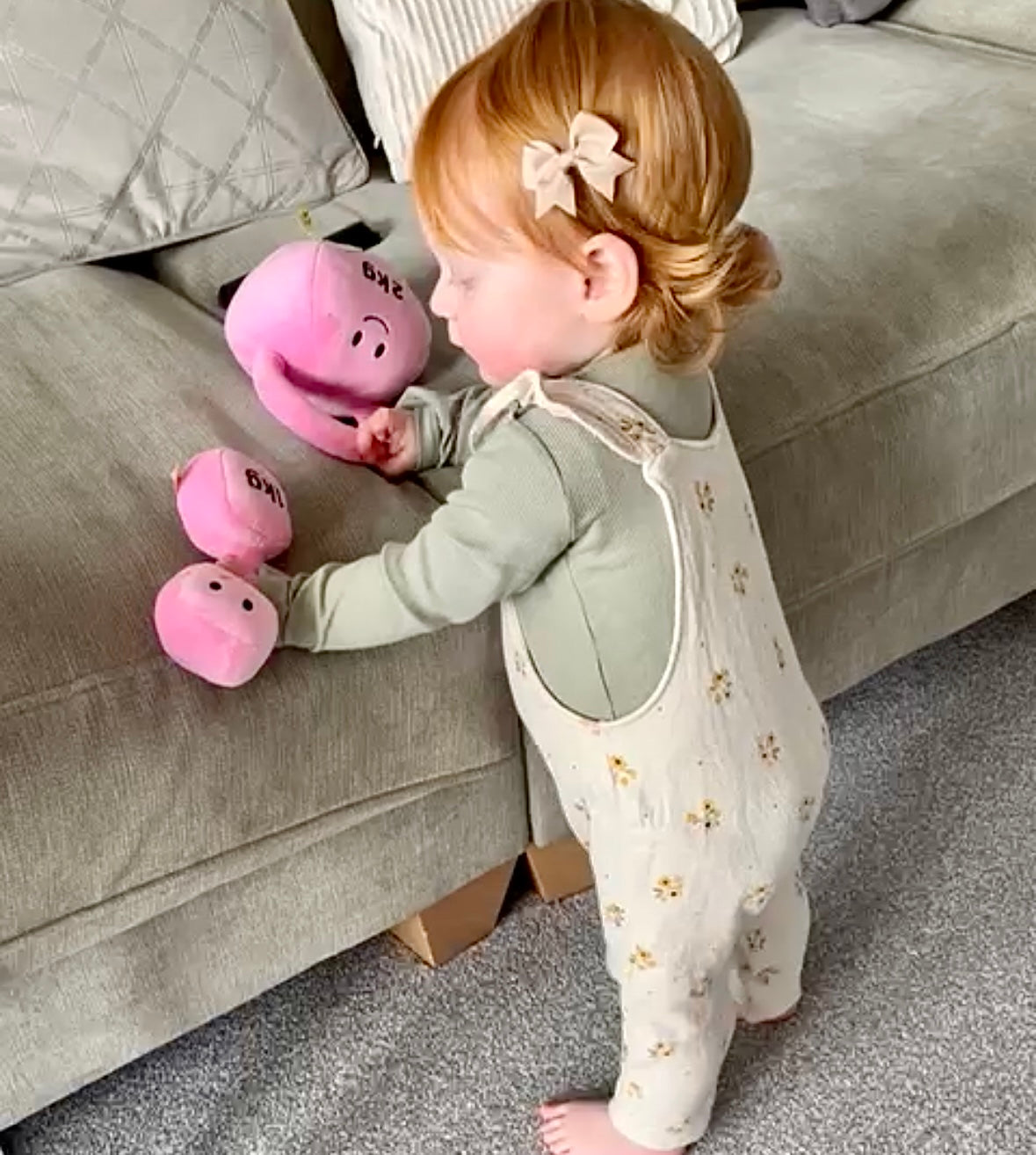 Toddler holding Hazza Toyz Candy Chateau Pink dumbbell and kettlebell on sofa, enjoying soft plush toys for sensory play and motor skills