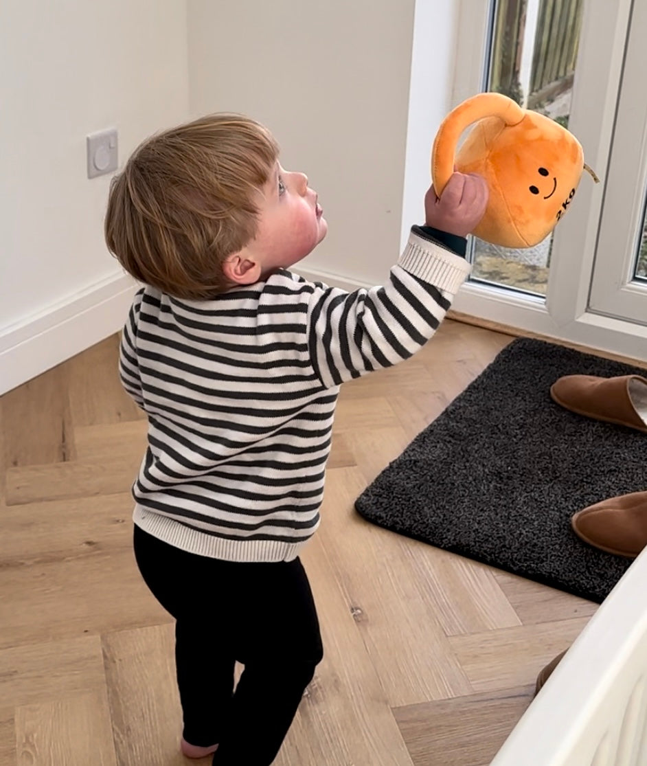 Toddler holding out arm with Hazza Toyz Apricot Orange kettlebell, engaging in playful interaction and motor skill development