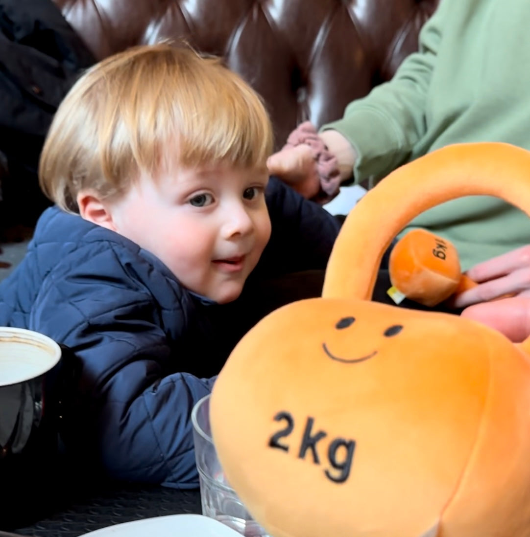 Toddler looking over at Hazza Toyz Apricot Orange kettlebell, showing curiosity and engagement with sensory play toy