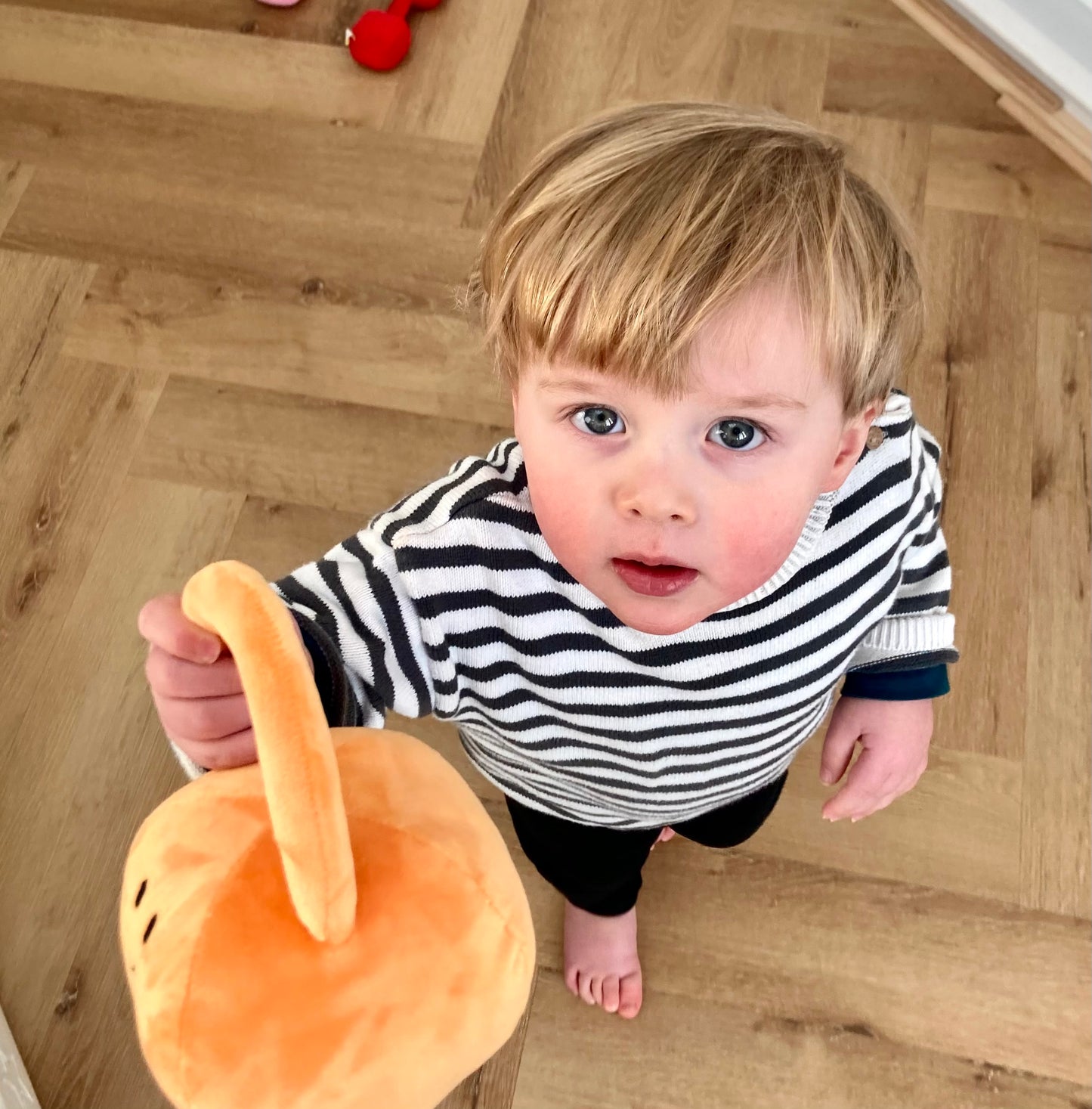 Toddler looking up at camera while holding Hazza Toyz Apricot Orange kettlebell, enjoying playful interaction and sensory engagement