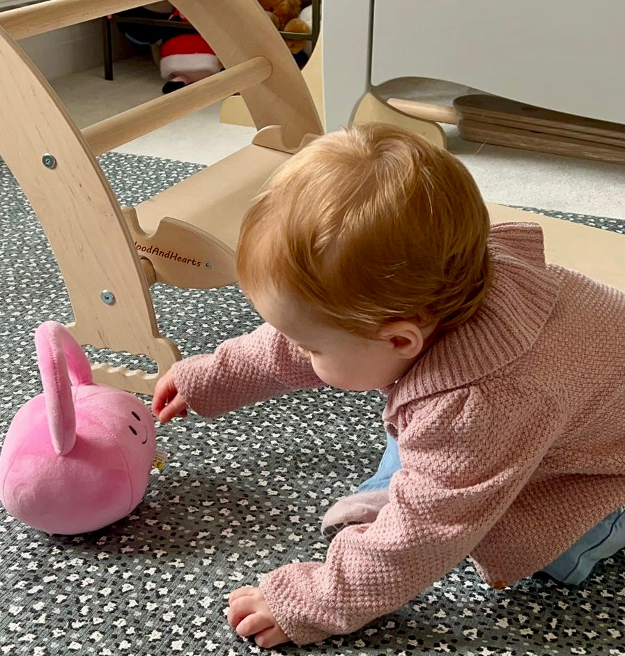 Toddler reaching for Hazza Toyz Candy Chateau Pink kettlebell, engaging in sensory exploration and motor skill development
