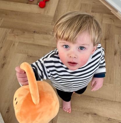 Toddler reaching up while holding Hazza Toyz Apricot Orange kettlebell, engaging in playful movement and sensory exploration