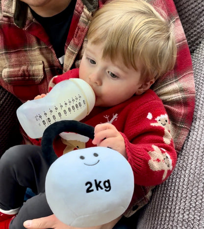 Toddler with dad, drinking milk from a bottle while holding Hazza Toyz Lamby Black and White kettlebell, enjoying a cosy bonding moment