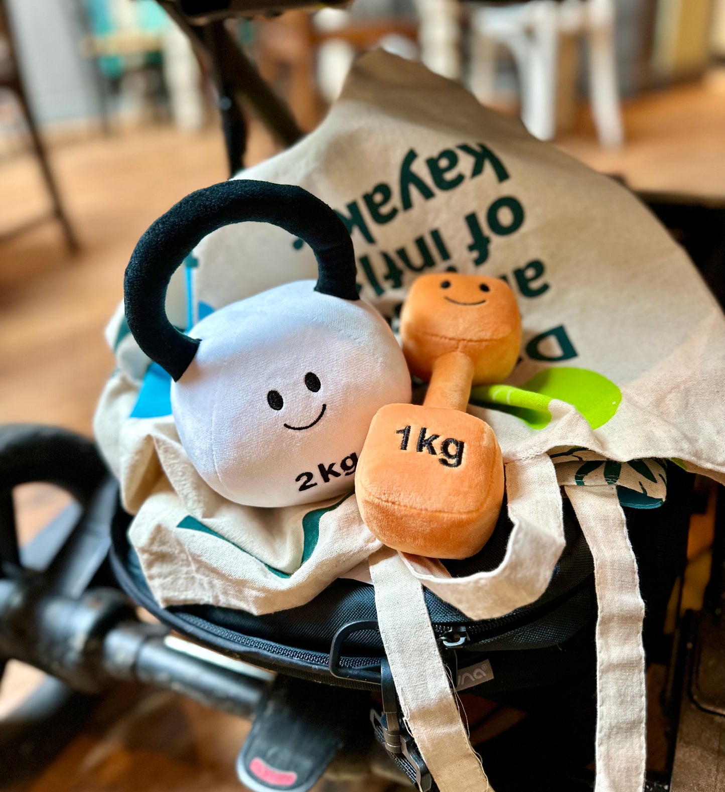 Hazza Toyz Lamby Black and White kettlebell and Apricot Orange dumbbell placed under a pram, ready for on-the-go sensory play