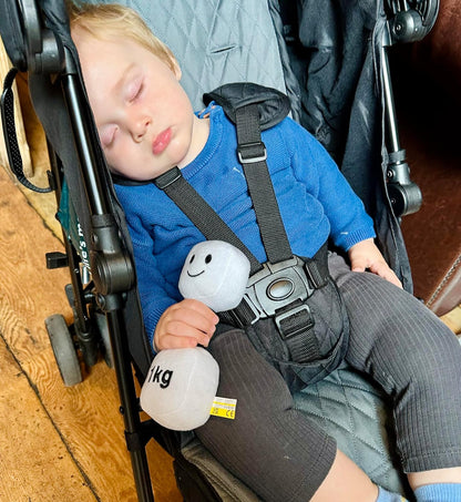 Baby asleep in a pram at a coffee shop, holding a Lamby Black and White dumbbell, capturing a peaceful moment with Hazza Toyz fitness-inspired toys for toddlers.